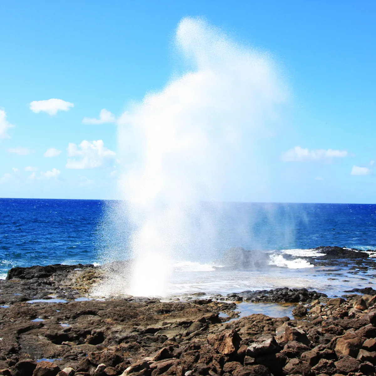 a body of water with smoke coming out of the ocean with Alofaaga Blowholes in the background