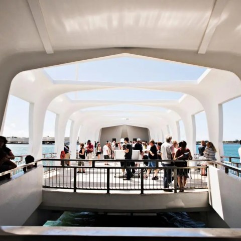 People inside a modern white architectural structure with large windows overlooking water.