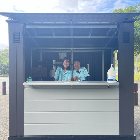 Two people in uniforms smiling at an outdoor kiosk.