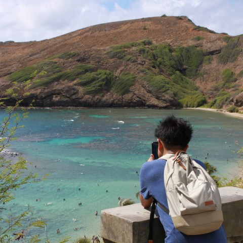 Person with backpack photographing a scenic beach view.